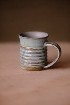 Secret Cenote Little Mug standing on a wooden surface with ribbed ridges and handle to the right.