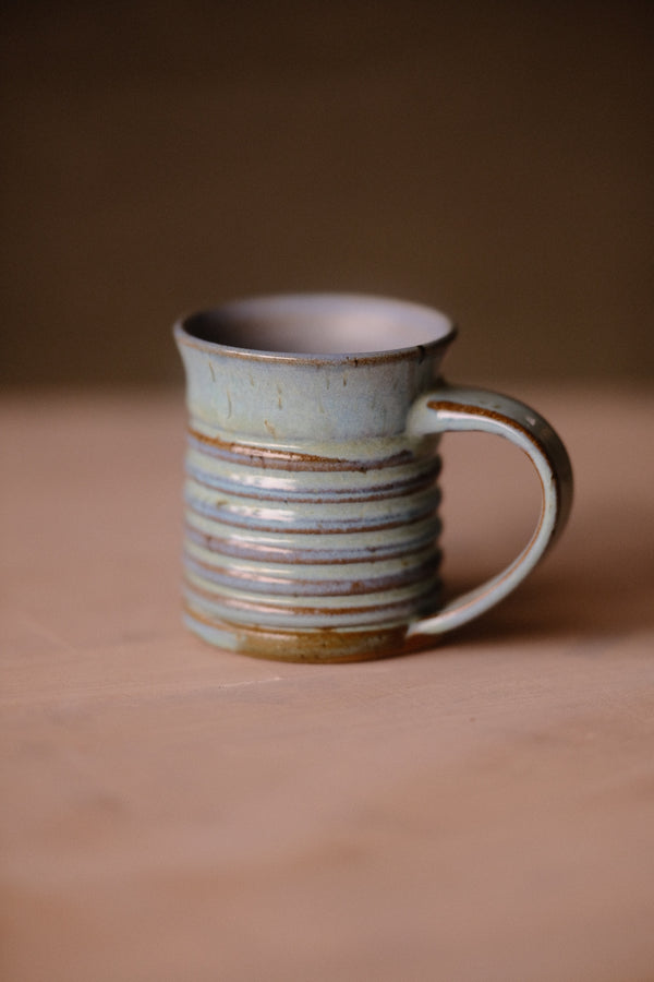 Secret Cenote Little Mug standing on a wooden surface with ribbed ridges and handle to the right.