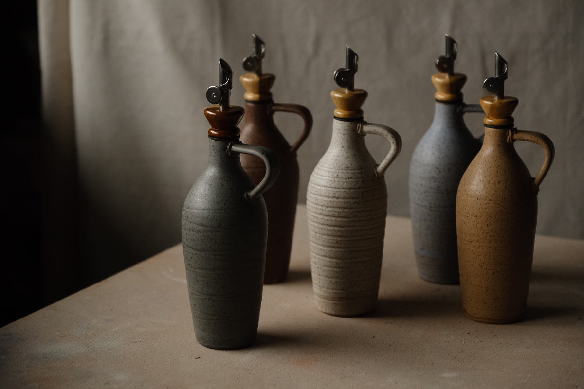 Tejas Oil Bottle collection of five cruets with loop handles and metal spouts, arranged on a studio surface.