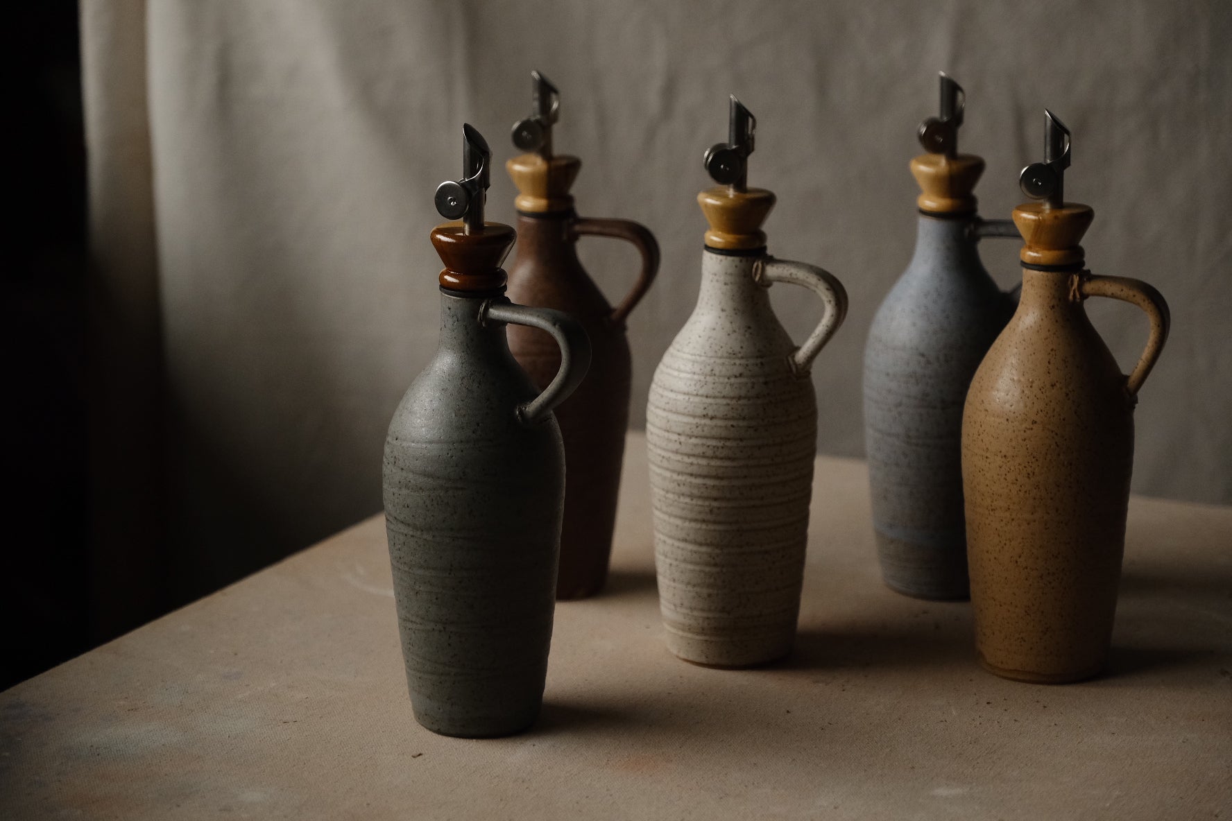 Tejas Oil Bottle collection of five cruets with loop handles and metal spouts, arranged on a studio surface.