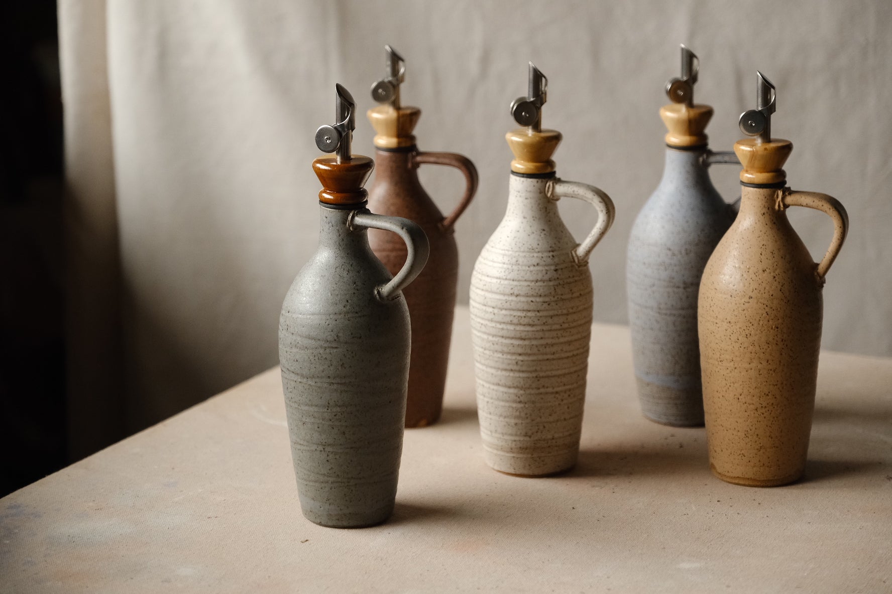 Tejas Oil Bottle group of five ceramic cruets in various neutral glazes, showing handles and metal spouts with wood collars.