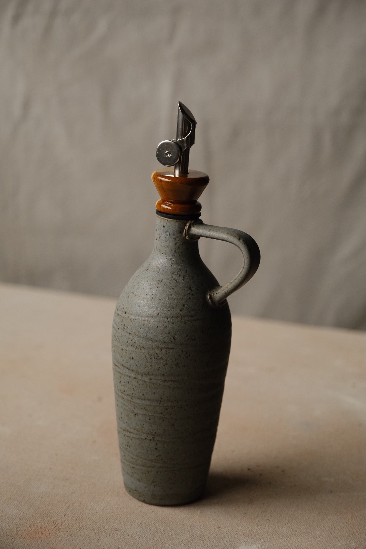 Tejas Oil Bottle in dark green-grey stoneware with subtle horizontal texture, loop handle, honey wood spout collar.