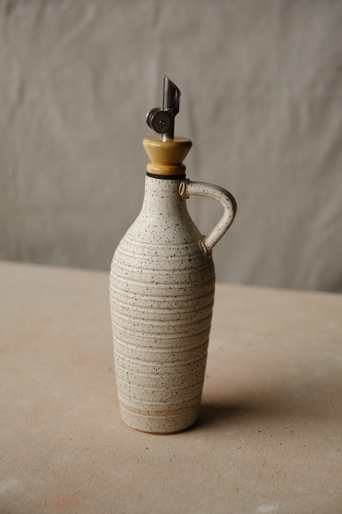 Tejas Oil Bottle in speckled cream stoneware with fine thrown rings, loop handle, metal spout with wood collar.