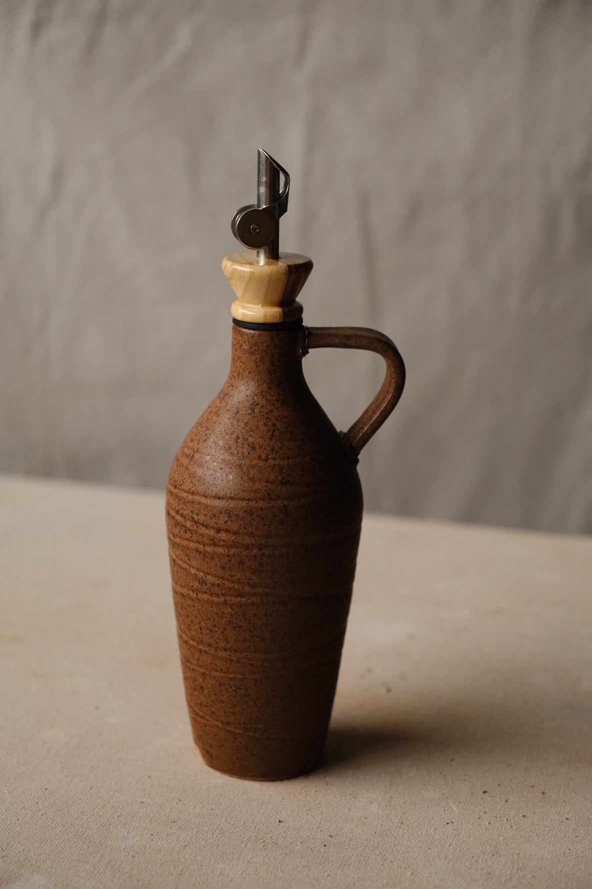 Tejas Oil Bottle in reddish brown stoneware with a handle, wood collar and metal pour spout.