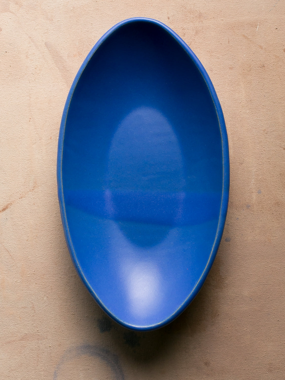 Wander Oval Server, top-down view of solid matte blue glazed stoneware dish on studio surface.