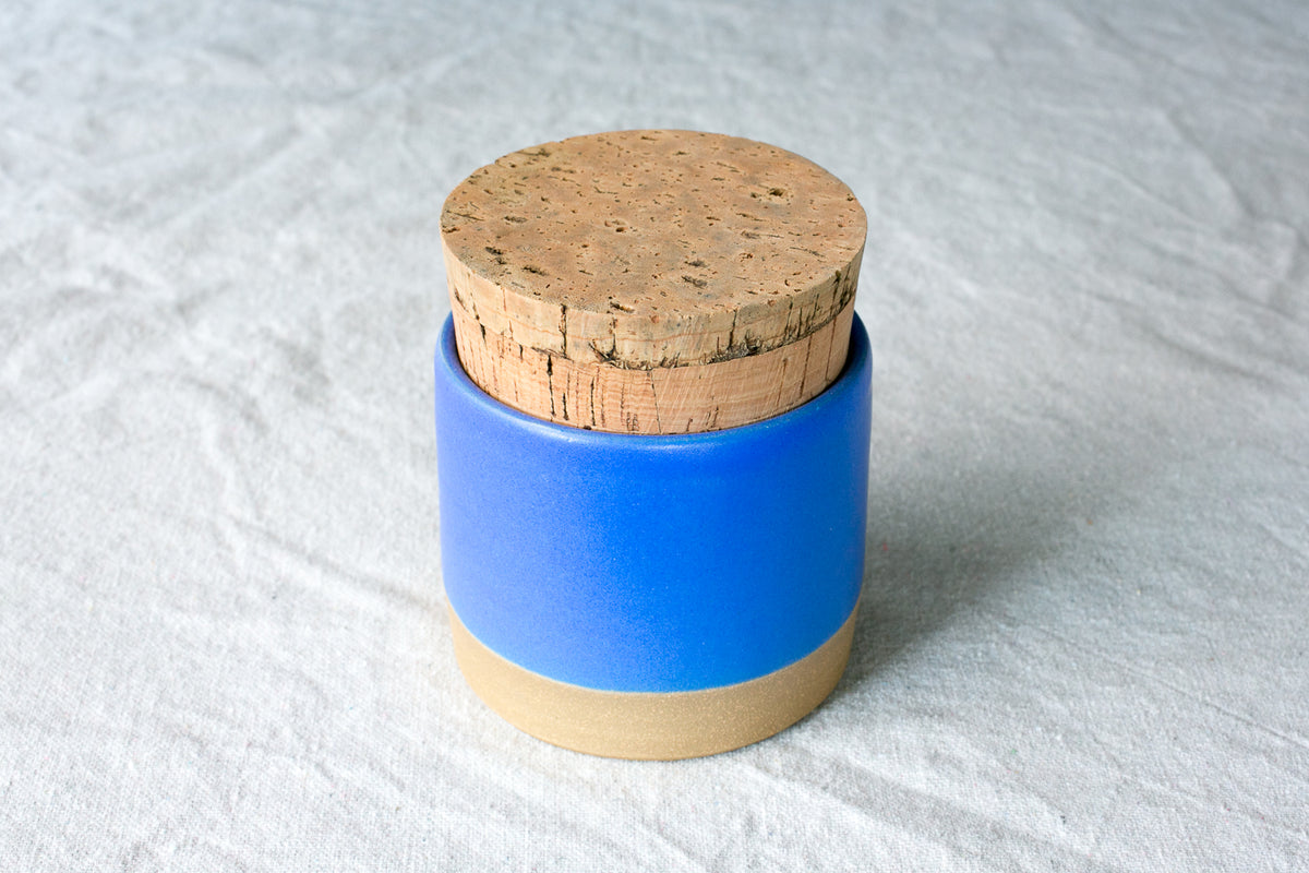 Wander Salt Jar in solid vibrant blue glaze with round cork lid and exposed clay foot on cloth.