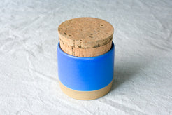 Wander Salt Jar in solid vibrant blue glaze with round cork lid and exposed clay foot on cloth.