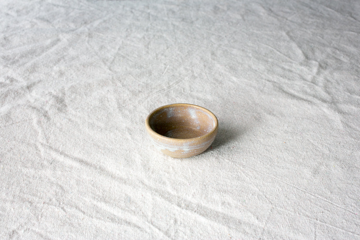 Wander Tiny Bowl in speckled brown glaze with a dusted white rim and exterior band, set on textured cloth.