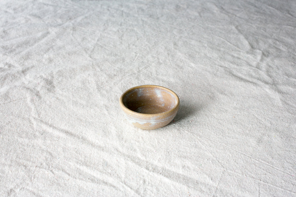 Wander Tiny Bowl in speckled brown glaze with a dusted white rim and exterior band, set on textured cloth.