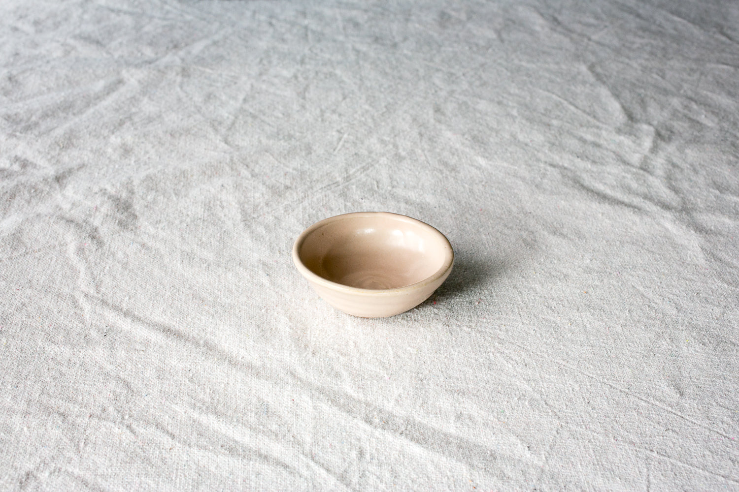 Wander Tiny Bowl in smooth glossy cream glaze, centered at a high three-quarter angle on textured cloth.