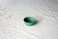 Wander Tiny Bowl in matte teal glaze with an exposed raw clay foot, viewed from above on textured cloth.