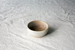 Wander Pinch Bowl, exterior in pale matte glaze with a mottled tan-amber pooled interior, elevated angle on linen.