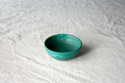 Wander Pinch Bowl in vibrant teal green glaze sitting angled on light woven linen cloth.