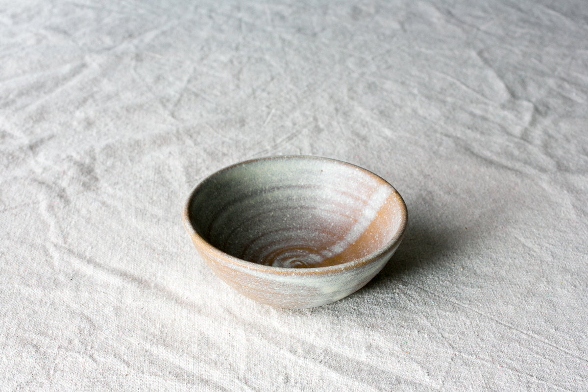 Wander Side Bowl in speckled neutral stoneware showing thrown interior rings on woven linen fabric.