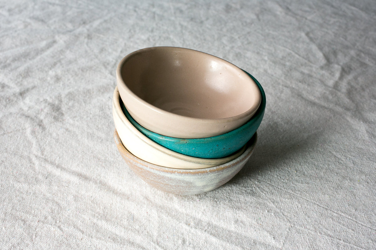Wander Side Bowl stack of four glazed stoneware dessert bowls nested at an angle on woven linen.