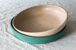 Two Wander Dinner Bowls, peach glazed bowl nested slightly angled inside a teal bowl on textured linen