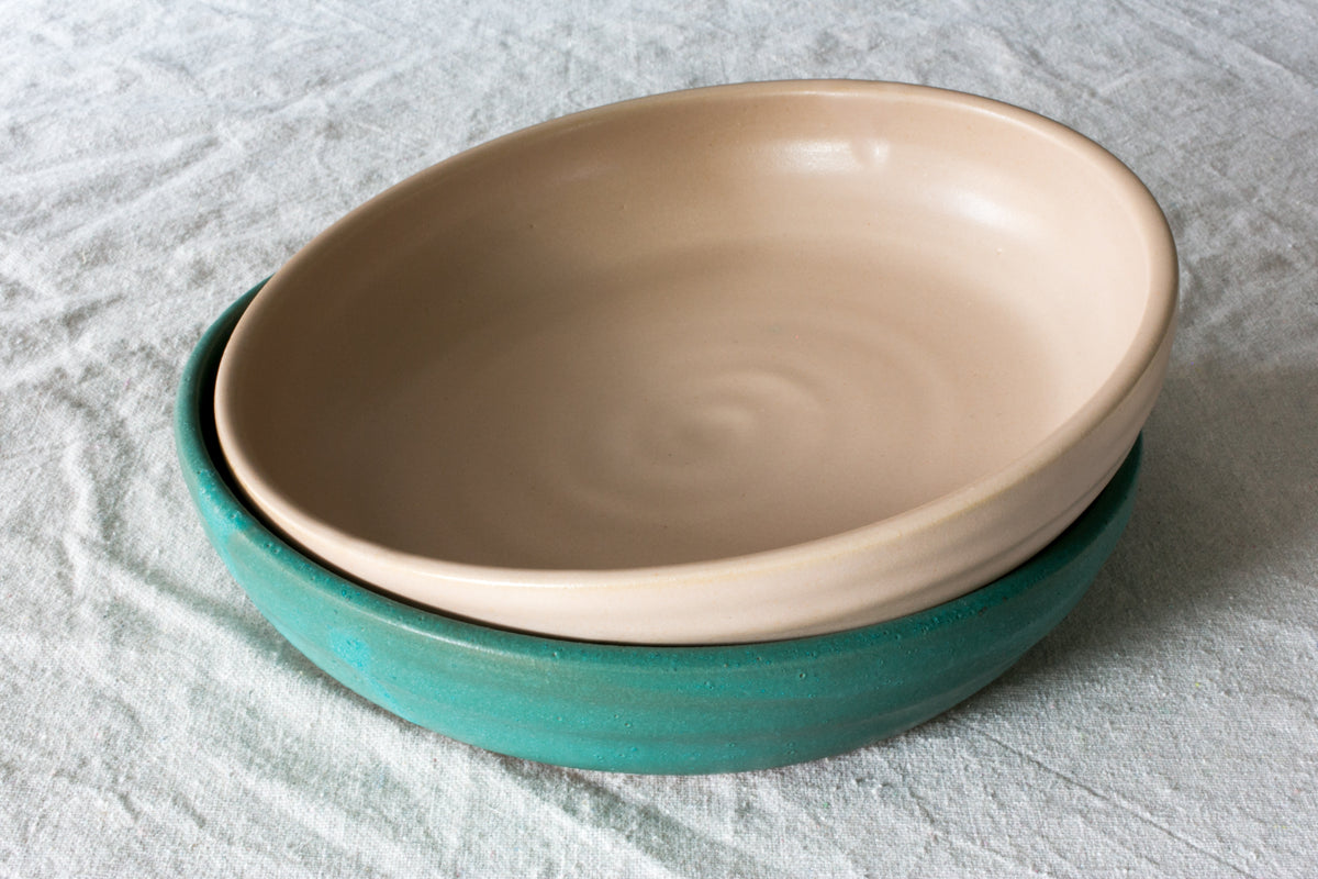 Two Wander Dinner Bowls, peach glazed bowl nested slightly angled inside a teal bowl on textured linen