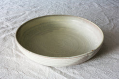 Wander Dinner Bowl in matte pale glaze, angled view resting on neutral textured cloth showing interior spiral ridges