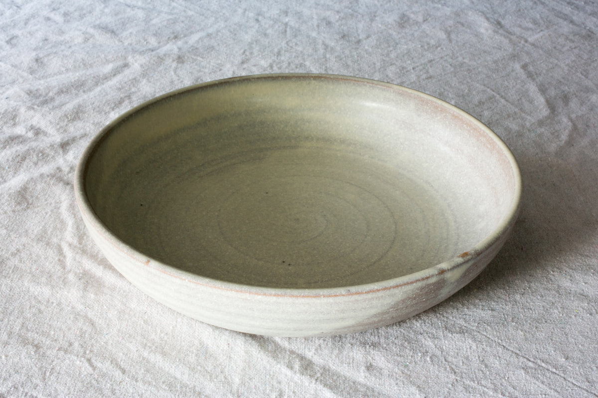 Wander Dinner Bowl in matte pale glaze, angled view resting on neutral textured cloth showing interior spiral ridges