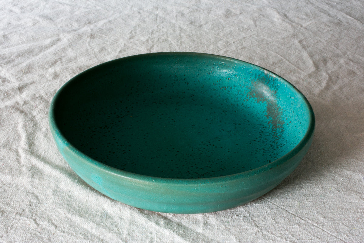 Wander Dinner Bowl with speckled teal interior glaze, angled view showing wide rim and shallow basin on cloth