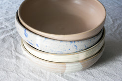 Wander Pasta Bowl stack of four ceramic bowls showing varied glaze finishes, set on linen.