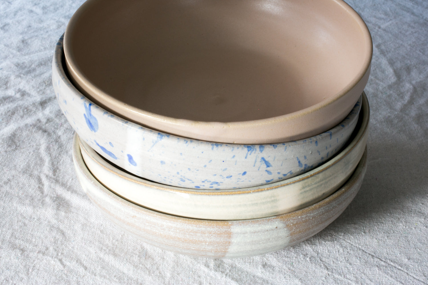 Wander Pasta Bowl stack of four ceramic bowls showing varied glaze finishes, set on linen.