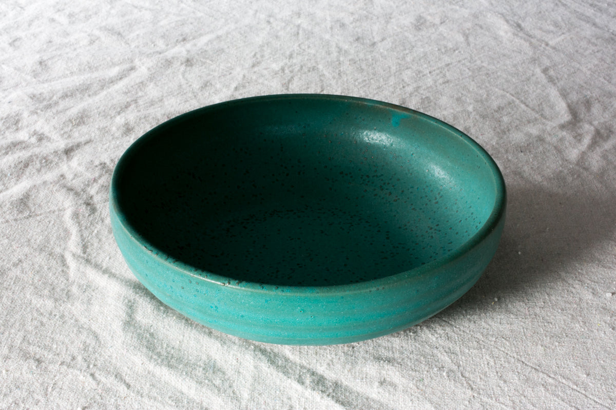 Wander Pasta Bowl in speckled turquoise glaze viewed from a high angle on woven linen.