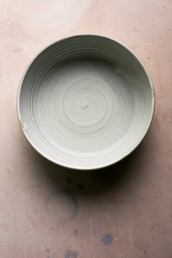 Wander Serving Bowl: top view of an off-white stoneware bowl with throwing rings, set on a studio surface.