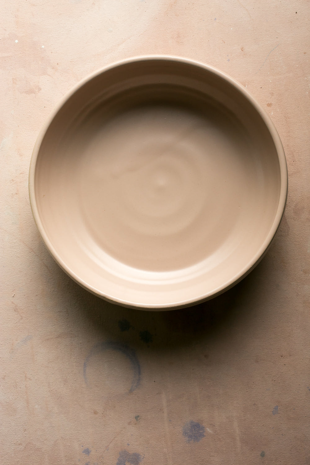 Wander Serving Bowl: overhead view of a warm beige stoneware bowl resting empty on a textured tabletop.