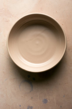Wander Serving Bowl: overhead view of a warm beige stoneware bowl resting empty on a textured tabletop.