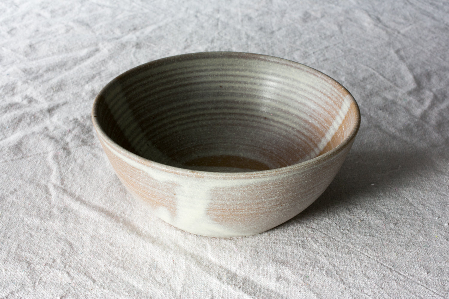 Wander Soup Bowl in two-tone dipped glaze with exposed throwing rings, resting on linen cloth.