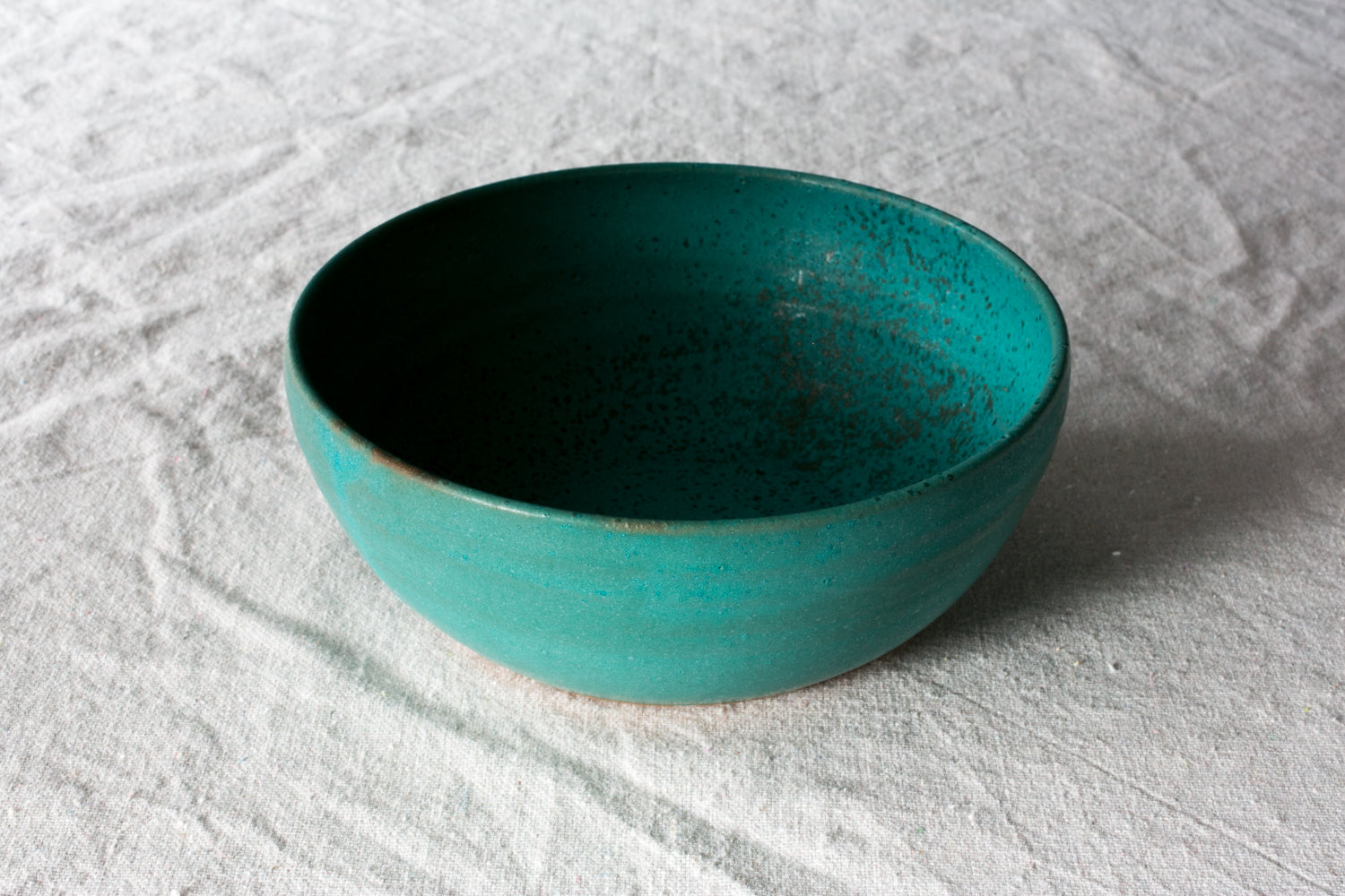 Wander Soup Bowl in bright teal matte glaze, angled view showing the smooth wide basin on linen cloth.
