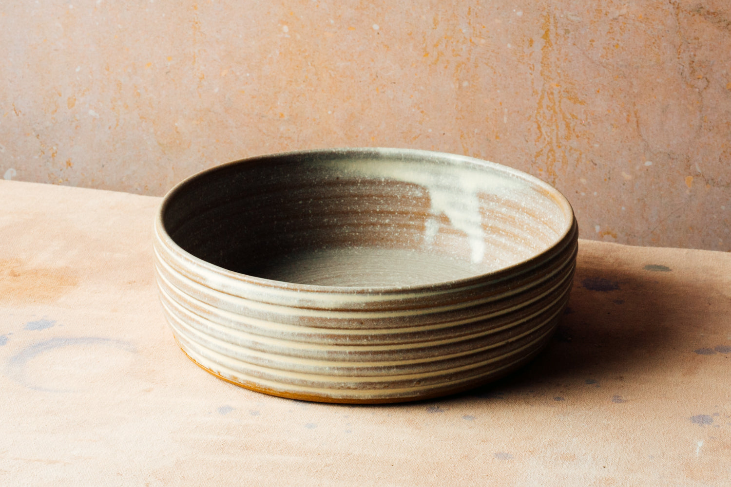 Wander Basket Bowl in light stoneware glaze with grooved exterior ridges on a speckled surface