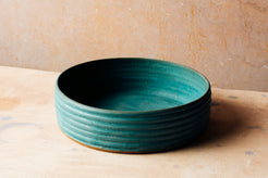 Wander Basket Bowl in teal glaze with exterior thrown ridges sitting on a speckled neutral surface