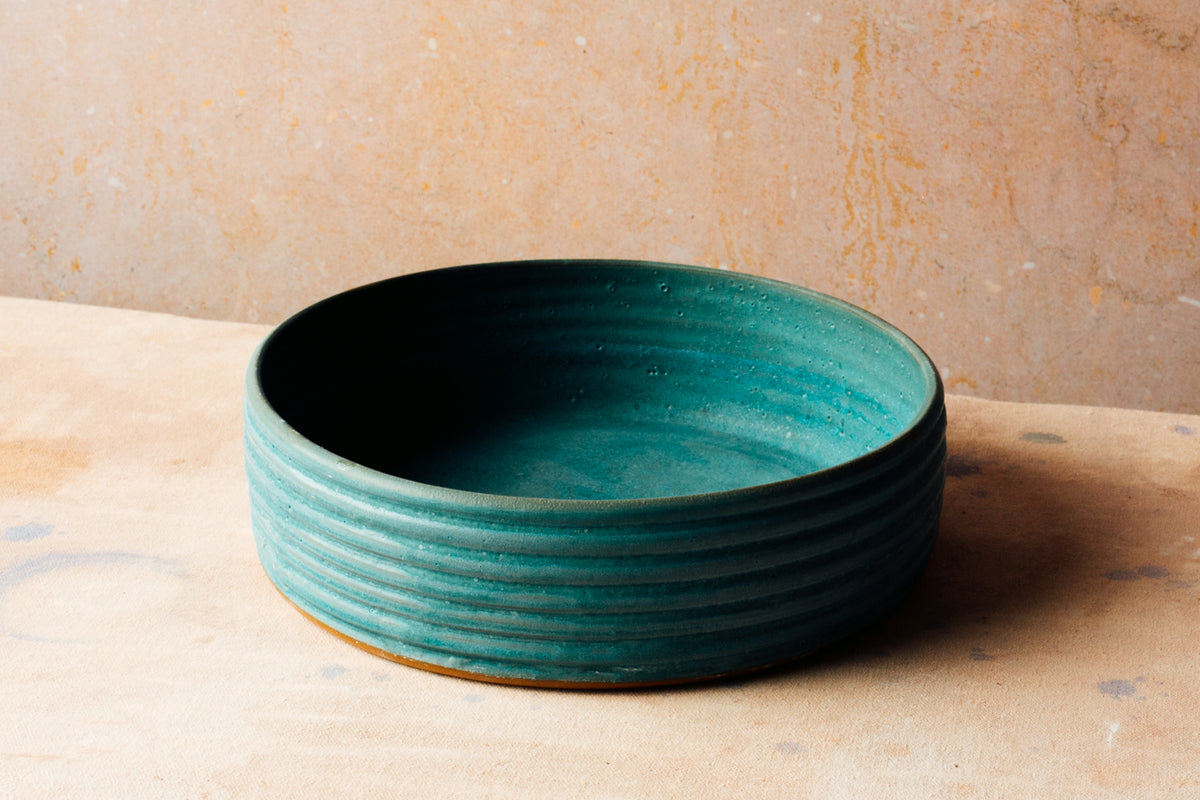 Wander Basket Bowl in teal glaze with exterior thrown ridges sitting on a speckled neutral surface