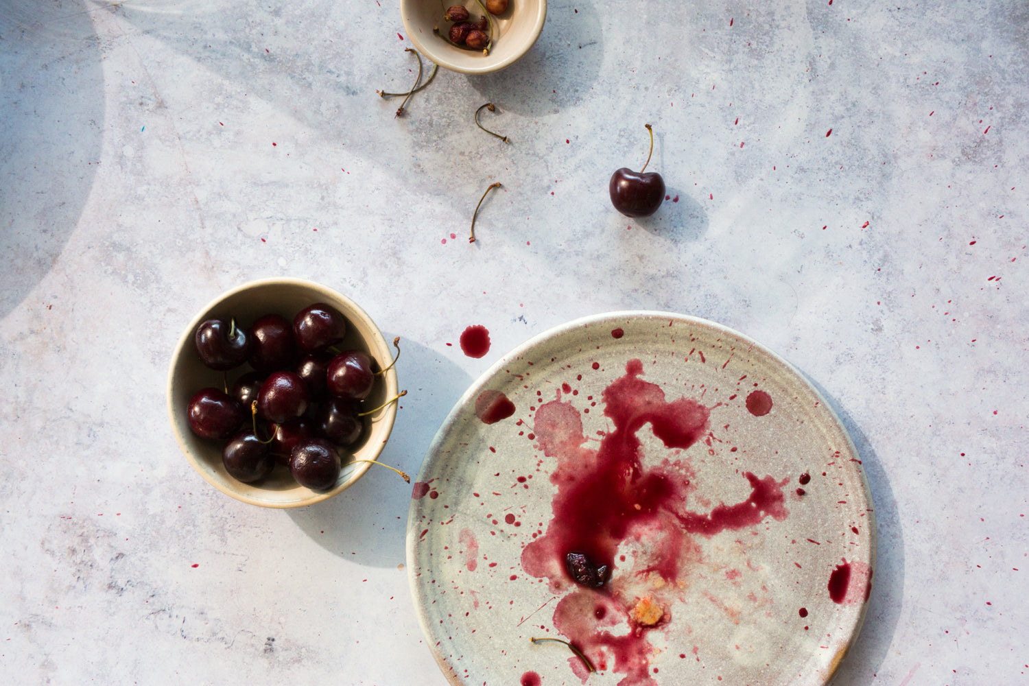 Horizon Lunch Plate with crushed cherry stains, next to a bowl of whole cherries and loose pits on a speckled surface.