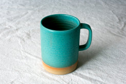 Wander Cappuccino Mug in bright turquoise glaze showing throwing ridges, side handle, and exposed raw clay foot.