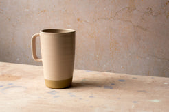 Wander Latte Mug in matte blush glaze, left-side handle and exposed raw clay base.