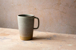 Wander Latte Mug in speckled matte grey glaze on canvas table with raw clay base.