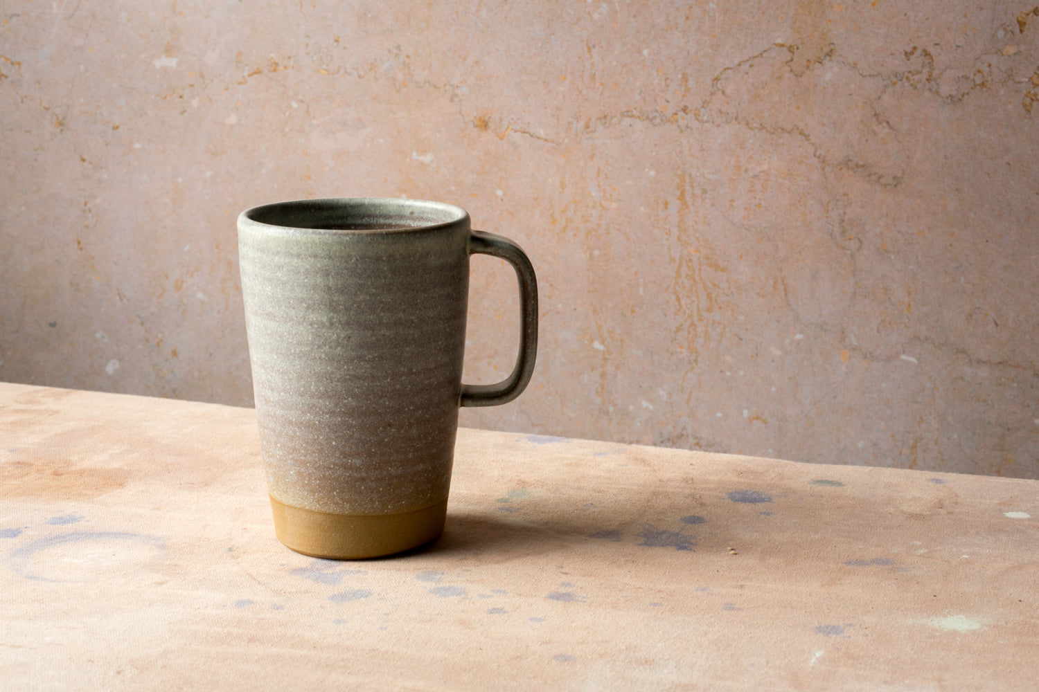 Wander Latte Mug in speckled matte grey glaze on canvas table with raw clay base.