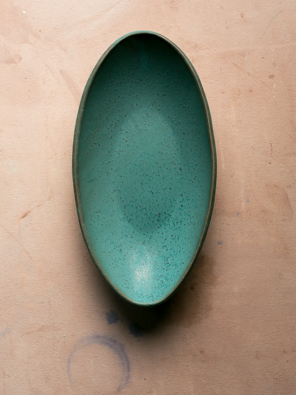 Wander Oval Server, top-down view of speckled green glazed dish resting on canvas.