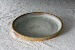 Fat Rim Dinner Plate with speckled grey-green glaze and bare stoneware rim, angled on linen.