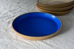 Fat Rim Dinner Plate with vivid blue glaze, resting on textured linen near a stack of ceramic plates.