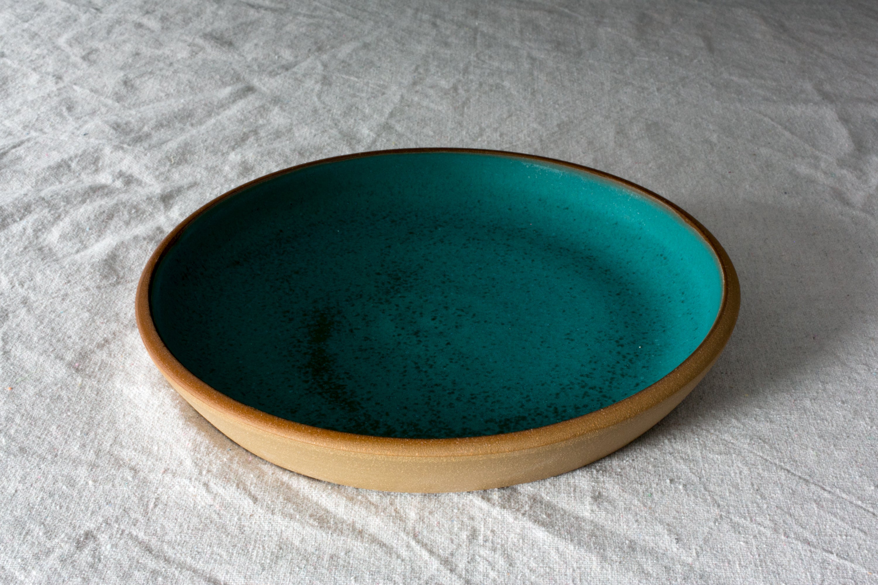 Fat Rim Dinner Plate in speckled teal glaze, showing the raised rim and flat interior on textured linen.