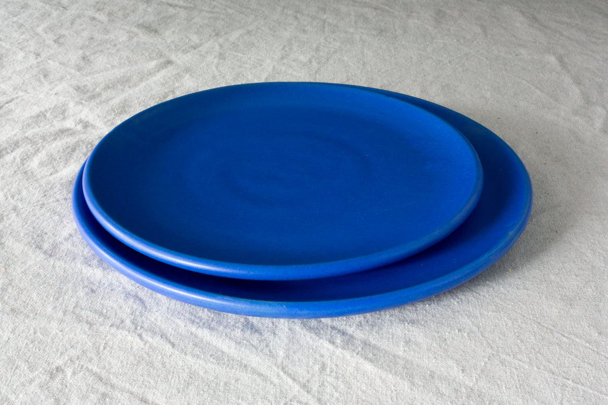 Horizon Lunch Plate stacked on a larger matching plate in a vivid royal blue matte glaze, resting on linen fabric.