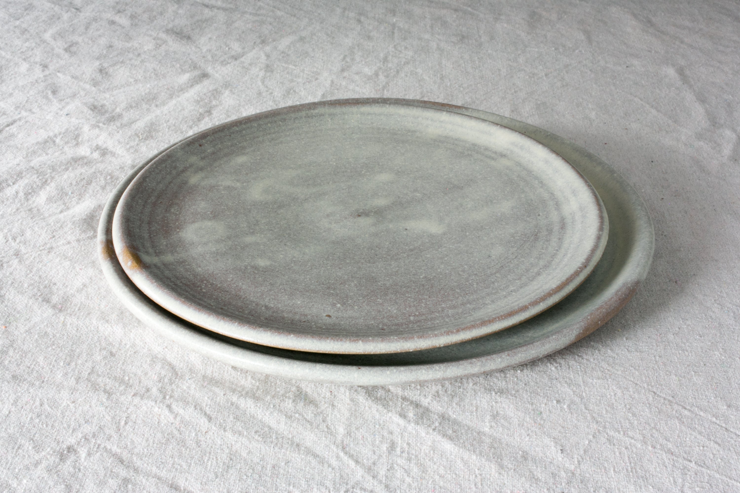 Horizon Lunch Plate stacked over a larger plate in a mottled matte gray glaze with a slight exposed raw rim, on linen.