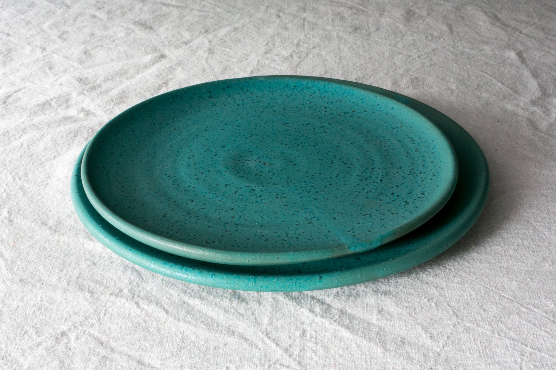 Horizon Dinner Plate: stack of two turquoise ceramic plates with subtle dark speckles on wrinkled cloth.