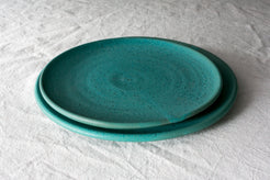 Horizon Dinner Plate: stack of two turquoise ceramic plates with subtle dark speckles on wrinkled cloth.
