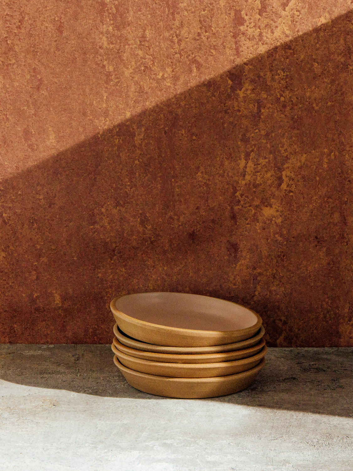 Fat Rim Dinner Plate stack of five pieces with blush glaze, set against a warm terracotta backdrop.