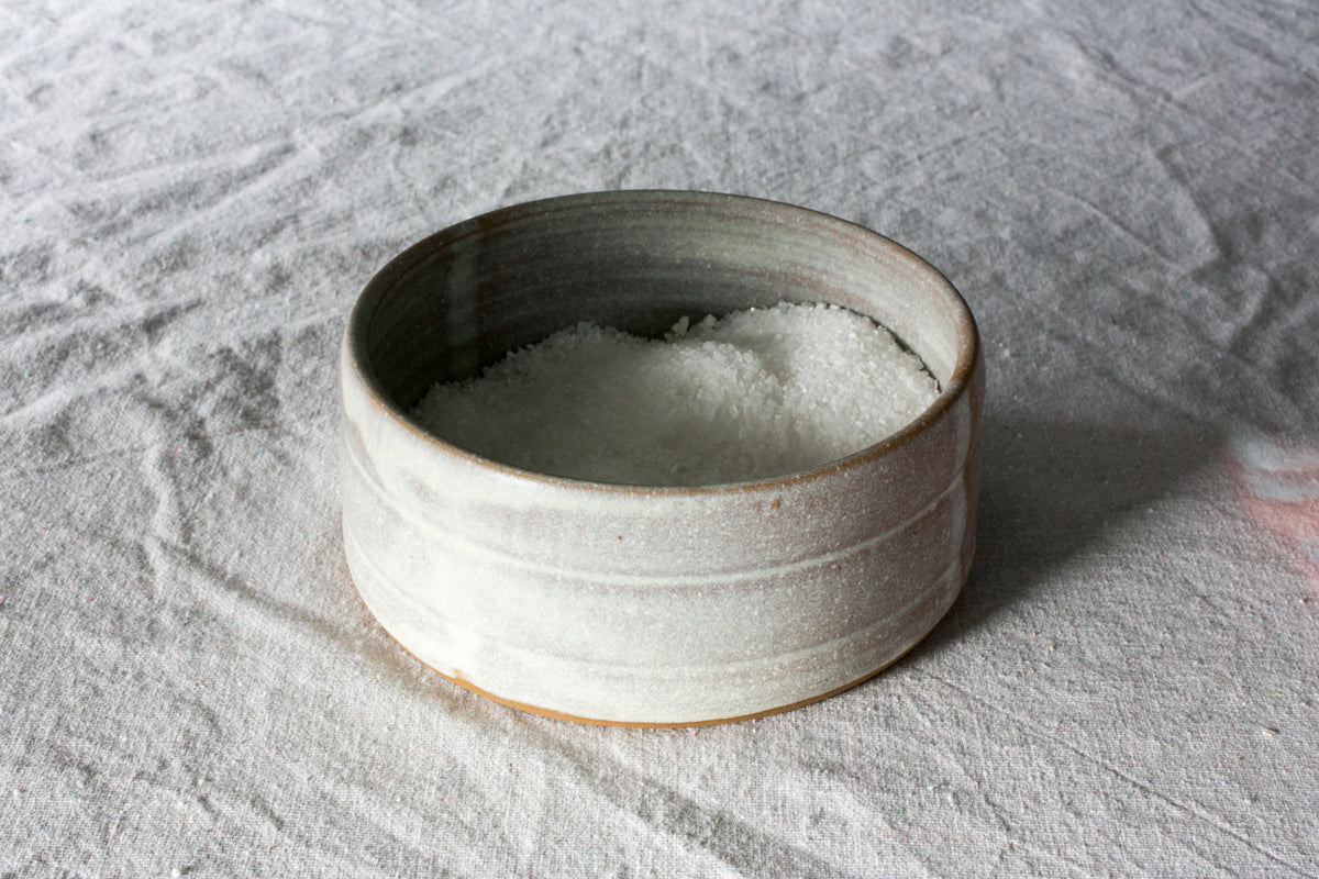 Wander Salt Pig: open-top white speckled ceramic dish filled with coarse salt, resting on wrinkled linen fabric.